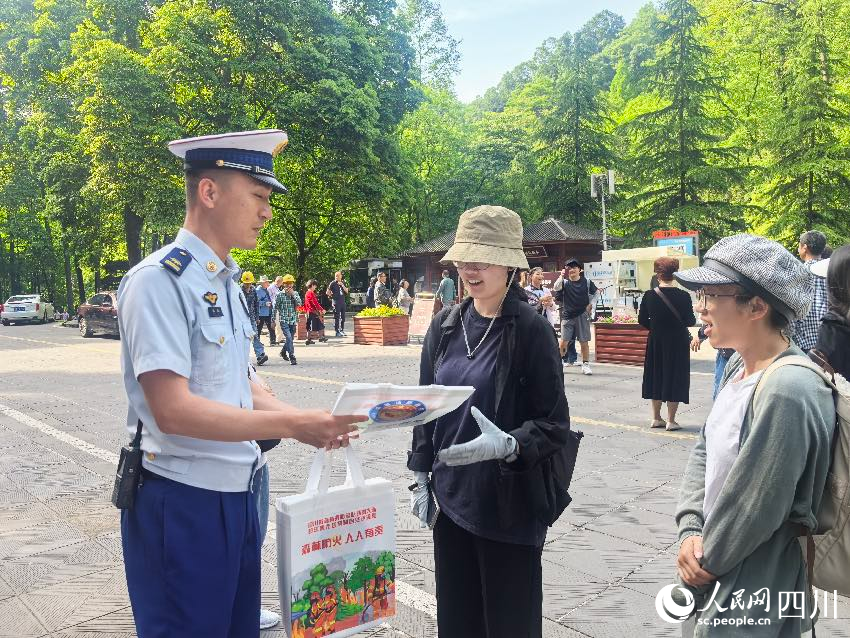 5月1日，青城山門口，消防員裴樂向游客發放防火宣傳單，普及森林防火常識。程雪力攝